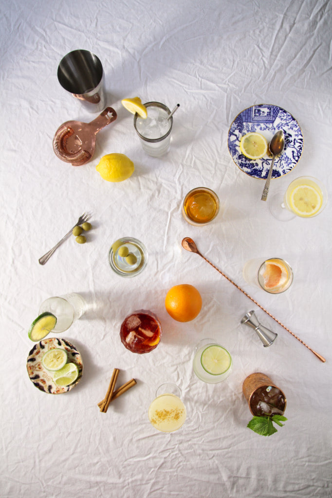 an overhead view of cocktails in glasses with tools on a white tablecloth